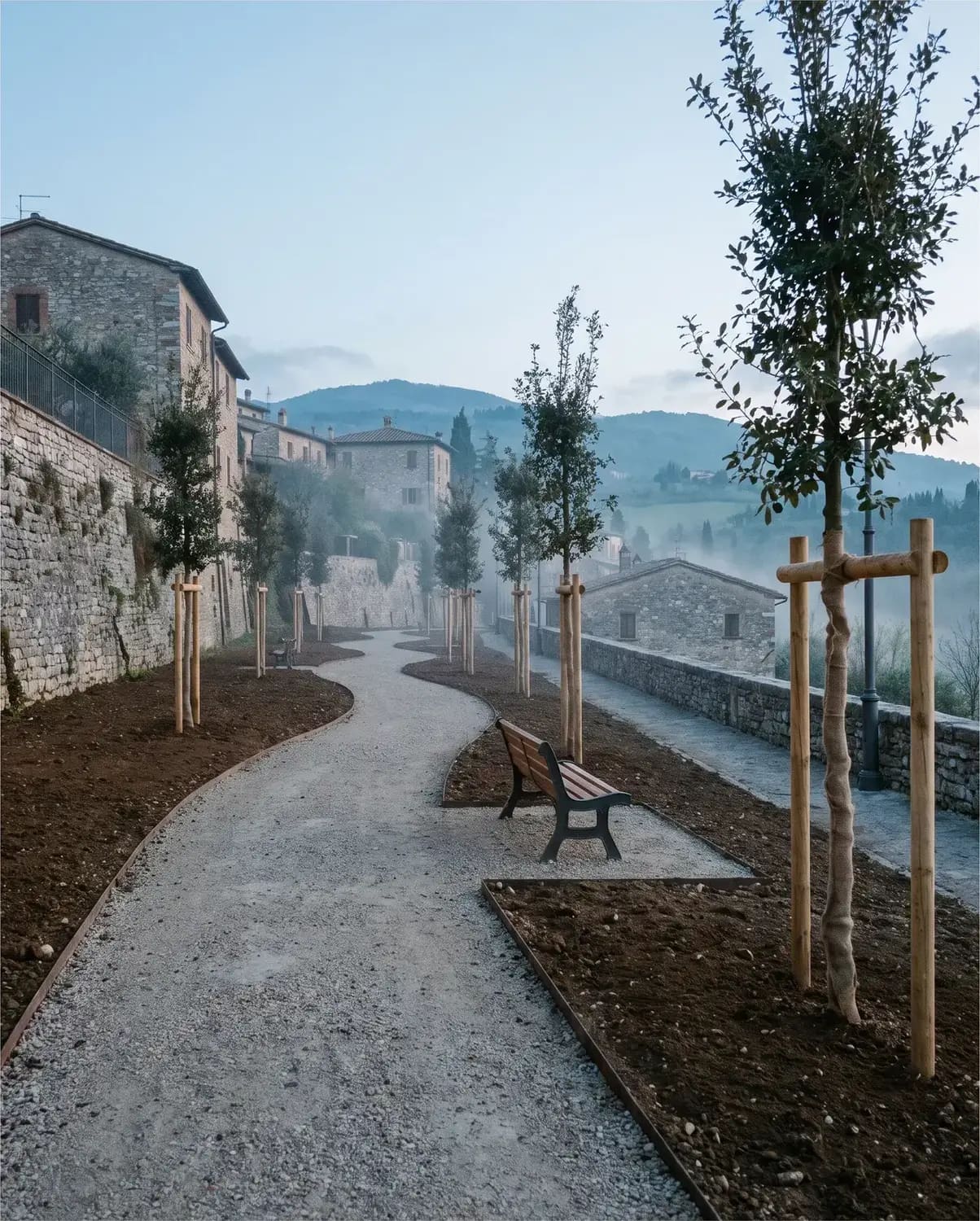 Un vialetto di parco appena risistemato, con alberi giovani e una panchina