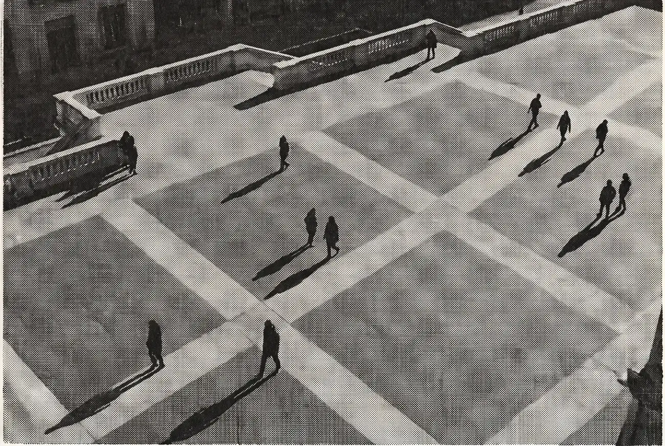 Una piazza pavimentata vista dall’alto, attraversata da figure minute